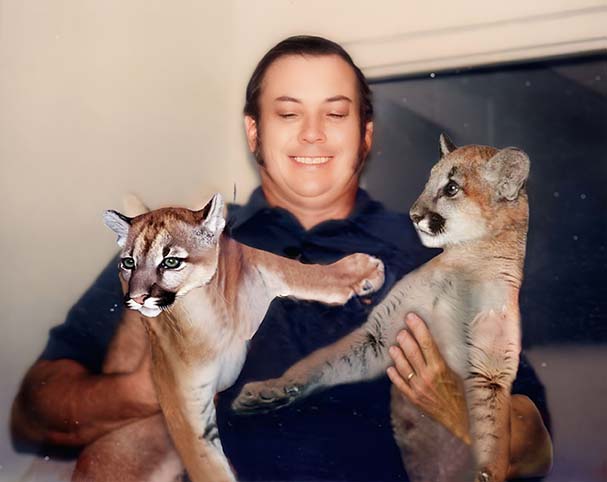 Man holding two cougar cubs after photo restoration process