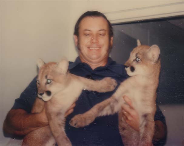 man holding two cougar cubs before photo restoration